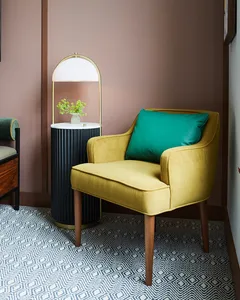 Modern living room with a yellow upholstered armchair featuring a green throw pillow, a marble side table with a brass lamp, 
