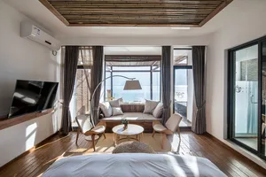 Modern residential bedroom featuring hardwood floors and upholstered furniture, with a view of the ocean and a seating area.