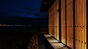 A modern residential exterior featuring wooden shutters and a stone pathway against a dark, starry sky.