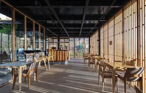Modern restaurant interior featuring wooden tables and chairs, with large windows allowing natural light to filter in.