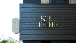 The exterior facade of a modern building with a black wooden exterior and a gold sign reading 'SAINT GEORGE'.
