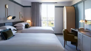 A modern hotel room with two double beds, a desk, and a window overlooking trees.