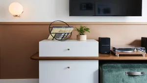 A modern living room featuring a white cabinet, wooden table, green ottoman, and a turntable with speakers.