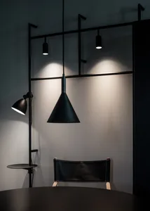 A minimalist office space featuring black metal pendant lights, a black leather chair, and a dark wooden table.