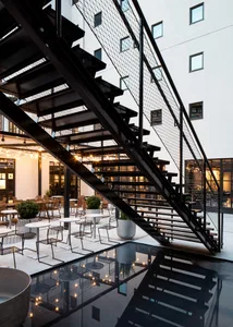 Modern industrial hotel lobby with a black metal staircase, glass walls, and concrete floor.