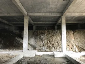 Concrete foundations under a building with exposed rock formations and construction debris.