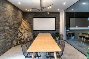 A modern industrial meeting room with concrete walls, wooden furniture, and a large white screen.