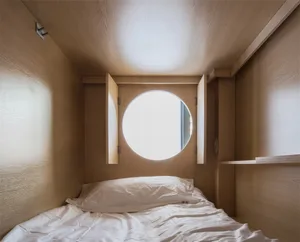 A minimalist bedroom with a bed and a round window in the ceiling, made of wood.