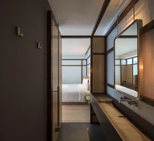 Minimalist bedroom with white bedding, wooden headboard, and concrete floors and walls.