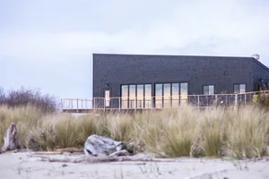 A minimalist beachfront house with black shingles and large glass windows.