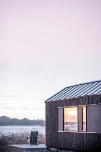 Minimalist design exterior of a cabin with wooden siding and a window reflecting the sunset.