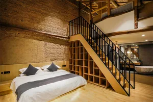 A modern bedroom featuring a double bed, grey pillows, a wooden headboard, and a floating wooden staircase with black railing