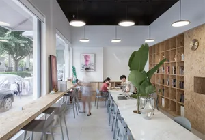 A modern cafe interior with a marble bar, wooden shelves, and metal stools.