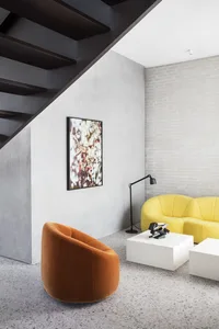 Modern living room with concrete floor, orange armchair, yellow sofa, and floor lamp.