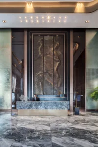Modern hotel reception area with marble floor and desk, featuring a large sculptural wall art piece.