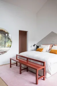 A modern minimalist bedroom featuring a concrete bench and a bed with yellow accent pillows.