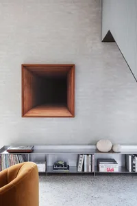 Modern minimalist living room featuring a concrete space with a dark wooden niche, a yellow armchair, and a shelf with books 