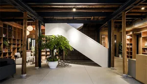 A minimalist lobby with concrete walls, large potted plants, and wooden structural elements.