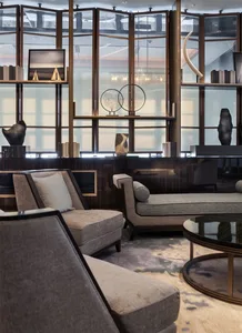 A modern living room with neutral-toned sofas and a coffee table, featuring decorative elements on shelves and a large window