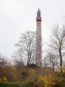 A tall, industrial concrete smokestack with red and gray stripes, surrounded by bare trees and autumn foliage.
