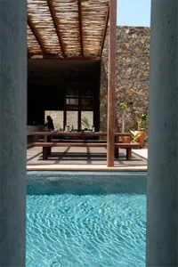 戶外休憩區設有木質餐桌，置於編織涼亭下方，前景為游泳池與石材元素