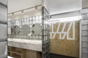 Modern, minimalist-style public toilet space featuring a white counter, glass-block walls, and a large sign that reads 'AASA'
