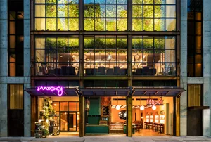 A modern cafe interior featuring concrete, glass, and greenery.