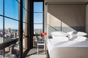A modern glass bedroom with a large bed and cityscape view through large windows.