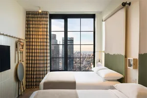 A modern hotel room featuring a city view, textiles, and a large window.