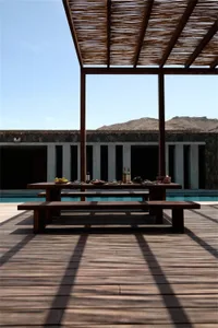 Outdoor wooden dining area with a table set for a meal, featuring a pergola and a scenic mountain backdrop.