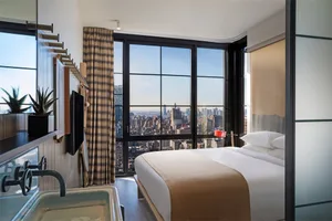 A modern residential bedroom with a city view through large glass windows.