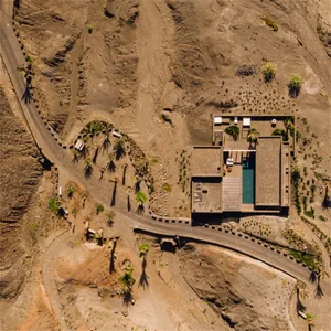 Aerial view of a modern, minimalist concrete house with a pool, located on a desert landscape.