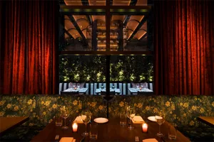 A restaurant dining room with red curtains, floral wallpaper, and candle-lit tables.