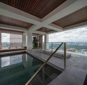 A modern indoor pool deck features concrete flooring and glass railings with a view of the cityscape.