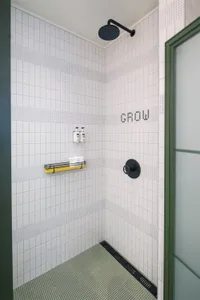 Industrial-style bathroom with white tiled walls, yellow shelf, and black shower faucet.