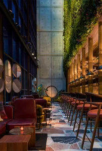 A modern bar with concrete walls, glass partitions, and wooden stools and tables.