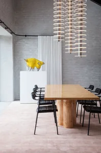 A modern dining room with timber table, black chairs, and a yellow art sculpture on a white pedestal.