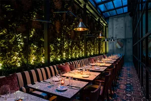 Modern restaurant with concrete, brick, and wooden elements featuring long tables and plush seating.