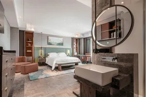 Modern bedroom with minimalist furniture, a large round mirror, a comfortable bed, and a vanity area with a rectangular sink 