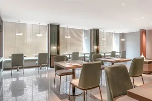 Modern minimalist design of a restaurant dining room with beige walls, wooden furniture, and pendant lights.