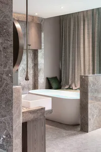Modern bathroom with marble walls and floor, featuring a freestanding bathtub and a sink with a wooden cabinet.