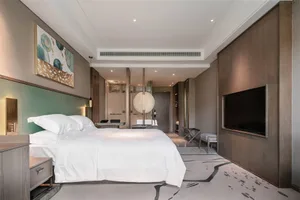 A modern minimalist bedroom with a clean white bed, green headboard, and artwork on the wall.