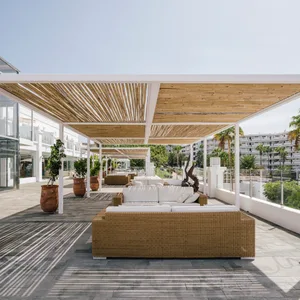 Outdoor lounge area with wicker furniture and white cushions under a wooden pergola.