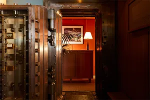 透過大型金屬銀行金庫門，望向工業風格的辦公室室內，展現金屬牆面與木質元素