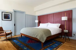 A modern bedroom featuring a wooden bed with a red headboard, white bedding, and a patterned rug on a wooden floor.