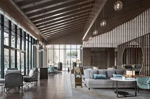 A spacious, modern industrial hotel lobby featuring glass walls, concrete flooring, and wooden accents.