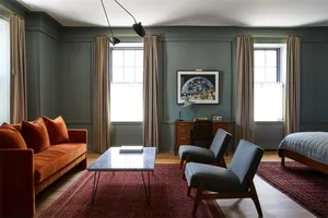A modern living room with an orange velvet sofa, two gray armchairs, a wooden desk, and a red rug.