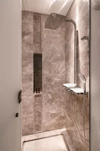Modern bathroom with marble walls, shower head, and shelf with bottles.