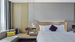 Modern minimalist bedroom featuring a white bed with purple accents, wooden headboard, and a grey upholstered bench.