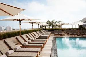Modern pool deck with wood lounge chairs and concrete planters, featuring white umbrellas for shade.